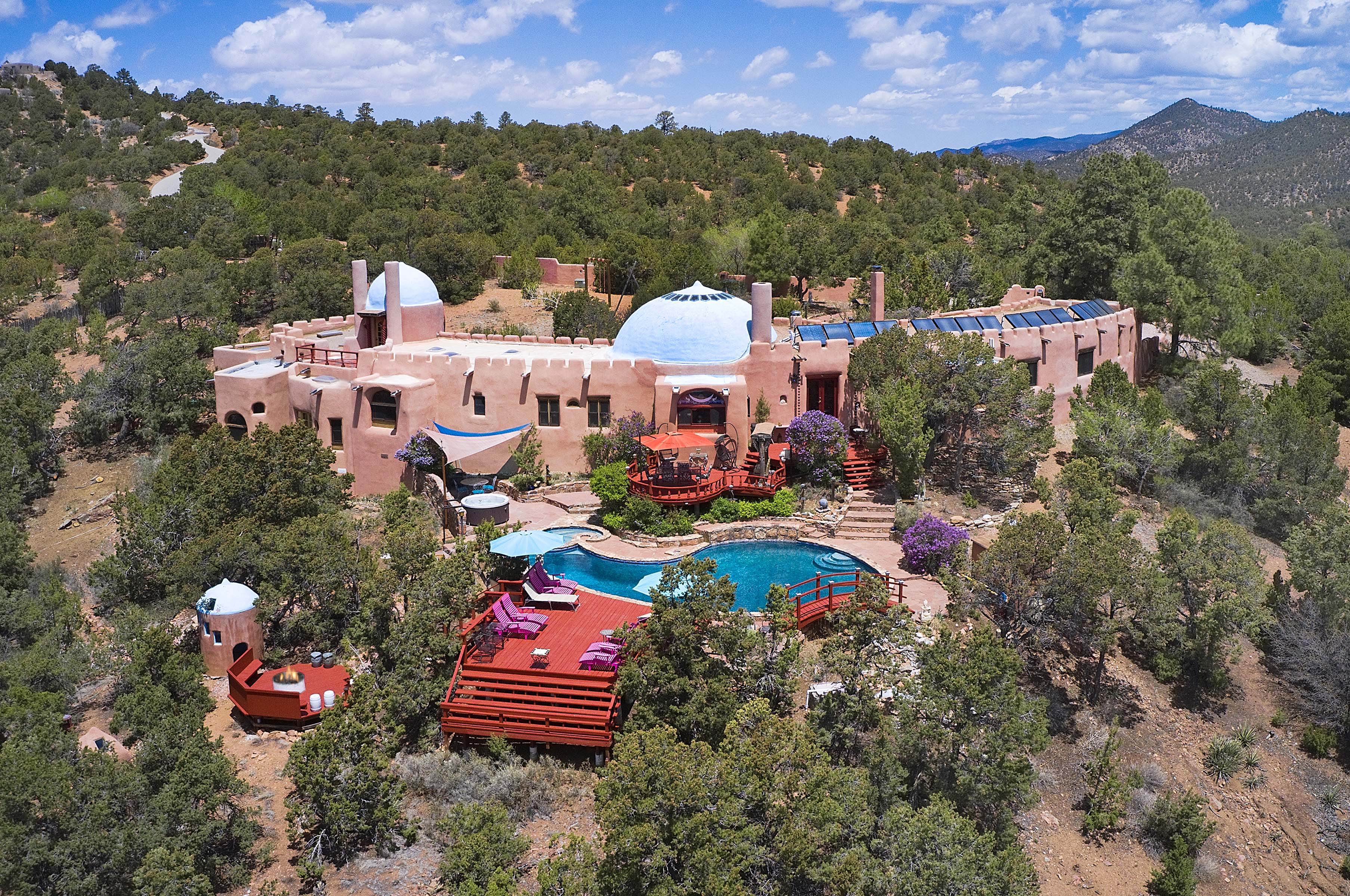 Aerial view of Rass Mandal Vacation Residence featuring a unique adobe structure with domed roofs, surrounded by trees and a swimming pool in the foreground.